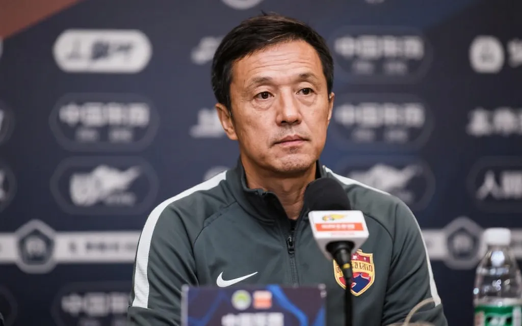 主帅在发布会上面对多个话筒与镜头，冷静回应提问的形象